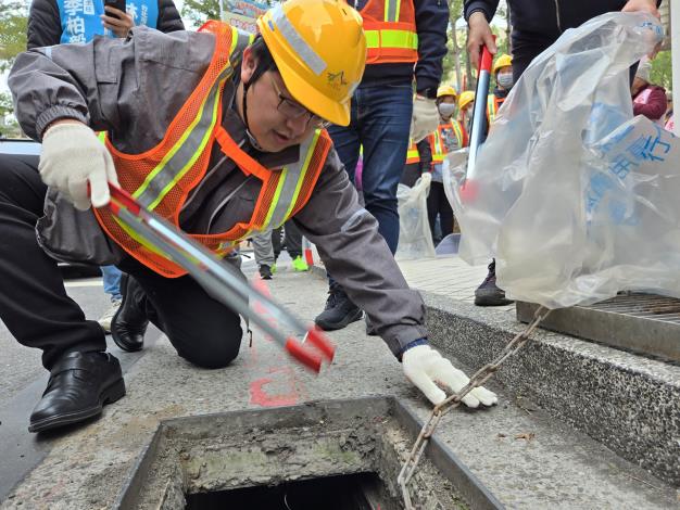 環保局局長徐世勲清除水溝蓋內菸蒂，並說明亂丟菸蒂對環境的危害