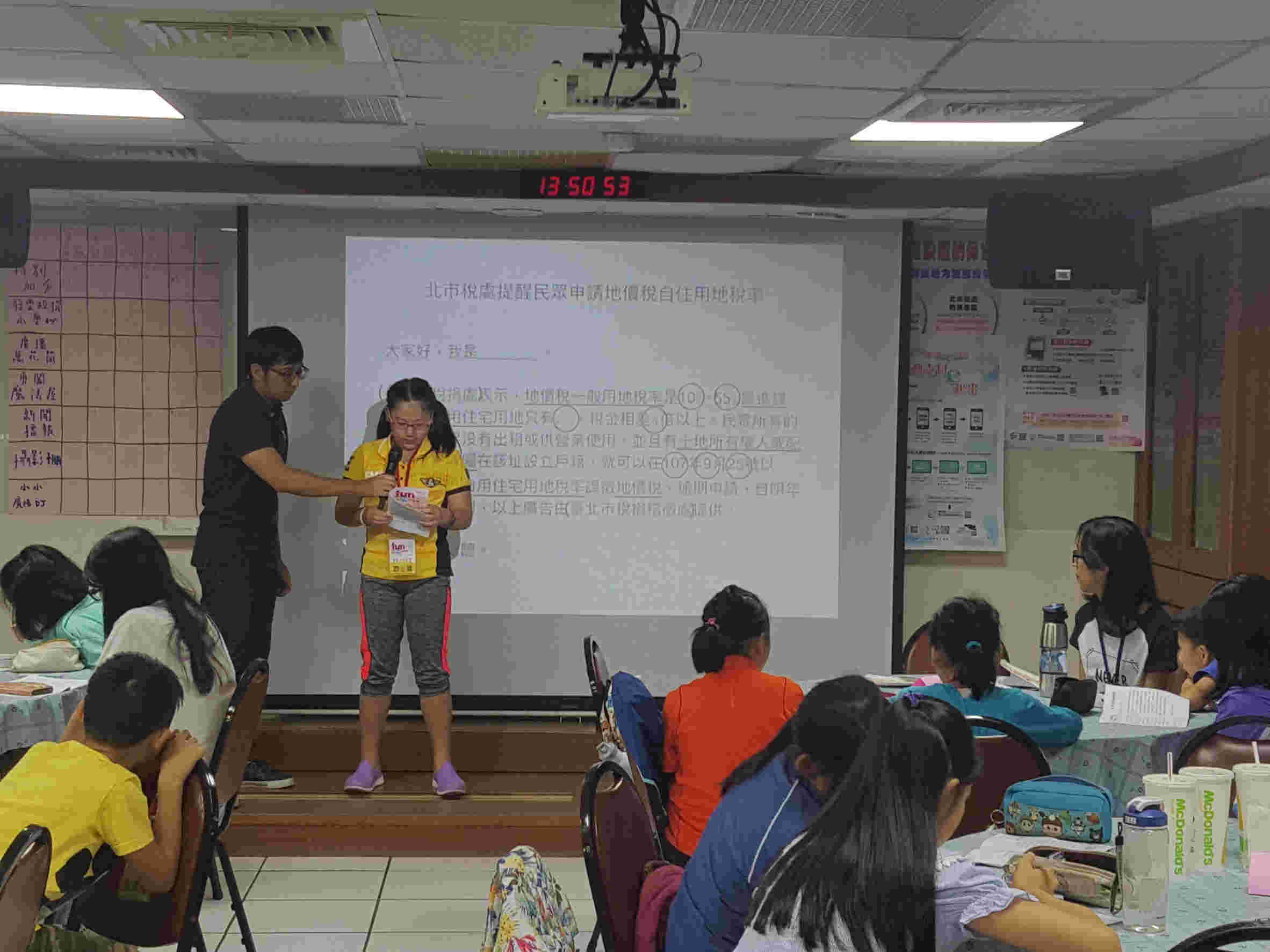 Boy and girl participants play broadcaster on stage.