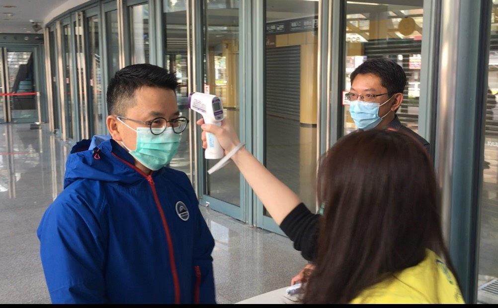 Staff takes the temperature of a visitor at the entrance of Taipei Arena