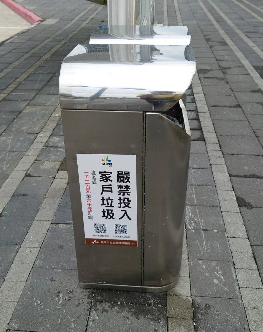 A roadside trash bin on the sidewalk