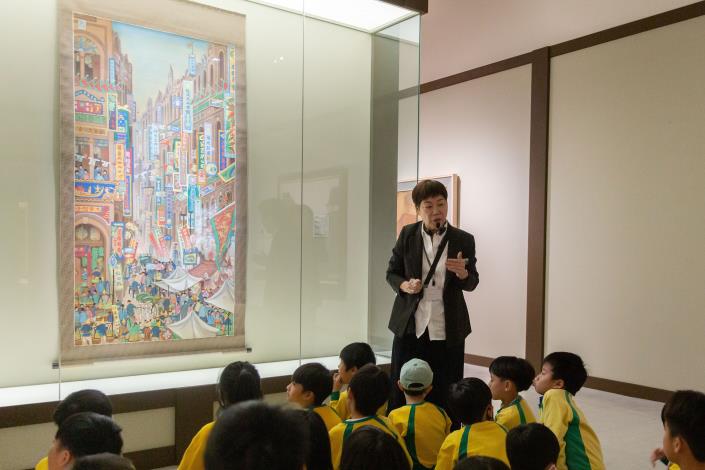 以美術館典藏的作品郭雪湖《南街殷賑》，讓學童認識臺灣在地畫家與帶領欣賞實際作品細節。