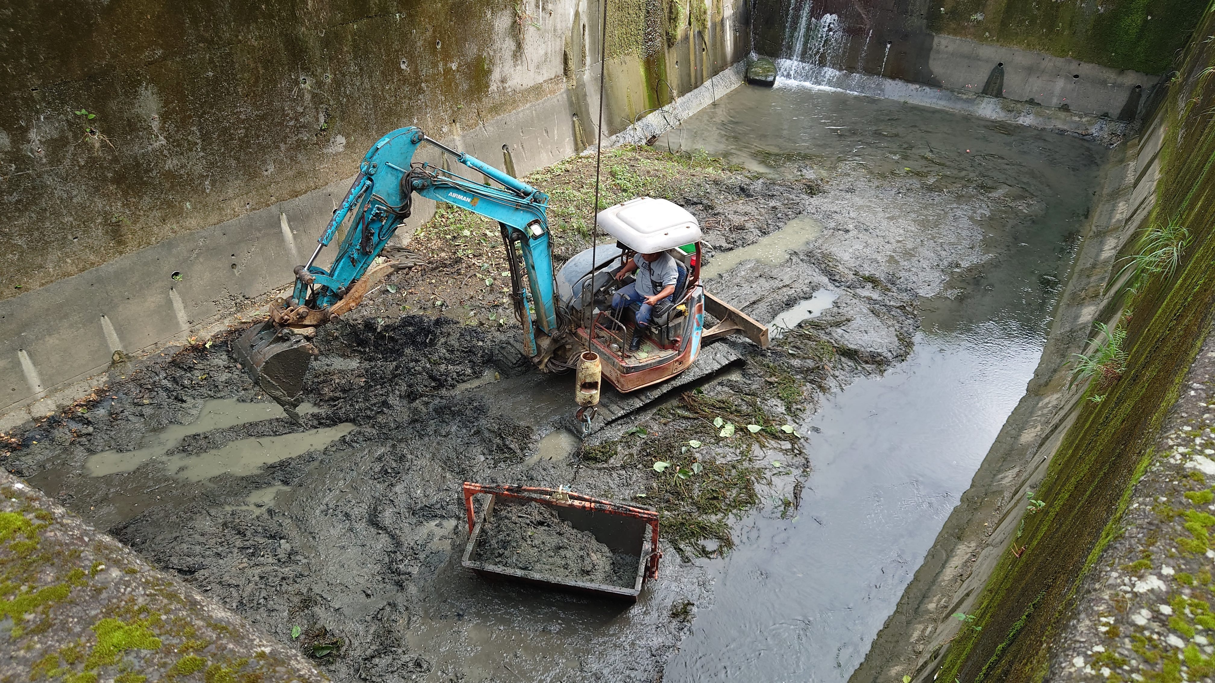 Workers removing muck from a silt detention basin